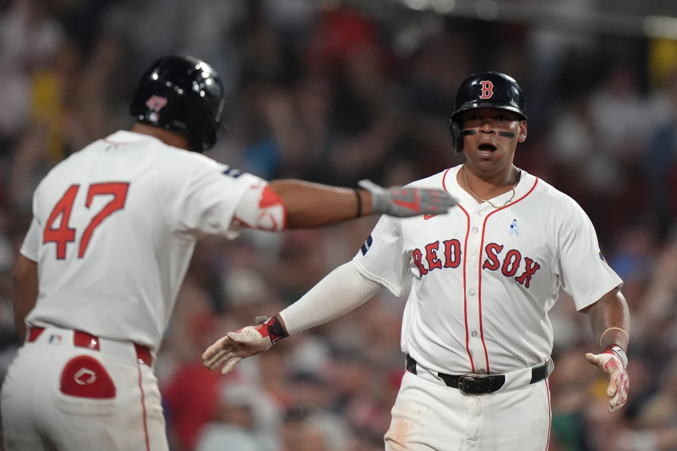 El dominicano de los Medias Rojas de Boston, Rafael Devers (derecha) celebra junto a su compatriota Emmanuel Valdez (izquierda), mientras regresa al banquillo luego de anotar en un triple de Connor Wong durante la séptima entrada del juego de béisbol ante los Yankees de Nueva York, el domingo 16 de junio de 2024, en Boston. (AP Foto/Steven Senne)